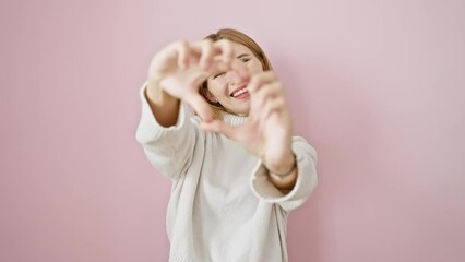 Canvas Print - Beautiful blonde girl, standing, hands shaping heart symbol in love. a romantic concept over pink isolated background. wearing winter sweater, blue eyes radiating happiness.