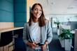 © Drazen - Young happy businesswoman in office looking at camera.