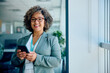 © Drazen - Happy mature businesswoman using cell phone in office and looking at camera.
