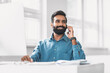Cheerful indian businessman talking on phone at office desk