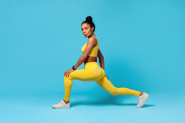 Wall Mural - African American fitness lady stretching legs lunging forward, blue background