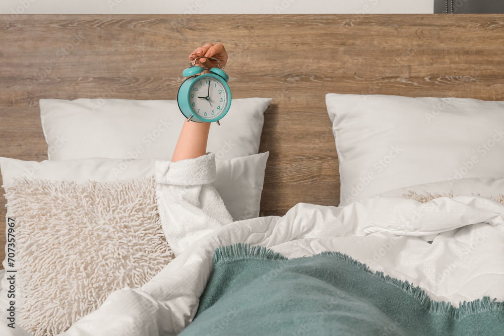 Woman in pajamas holding alarm clock while lying on bed