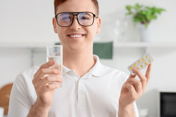 Sticker - Young man with glass of water and pills at home, closeup