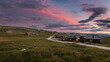 Huts in landscape of Rondane national park in Norway during sunset, road leading through green hills, clouds in the sky.