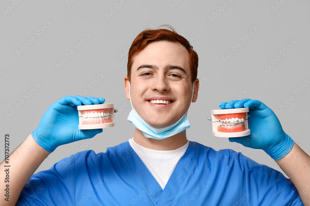 Male dentist with jaw models on grey background. World Dentist Day
