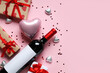 Bottle of wine with gift boxes, chocolate candies and heart shaped air balloon on pink background. Valentine's Day celebration