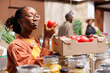 Detailed view of a young black woman holding and admiring a ripened red tomato in an eco friendly supermarket. Image showing an African American lady examining freshly harvested produce.