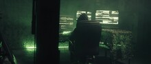 Hacker Sitting In The Dark Office And Typing Commands On Several Computer Monitors .Hacker Computer Screens Code. The Faceless Hacker  