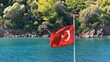 Turkish flag waving on the bow of the yacht on a boat tour. Gokova Bay which is mentioned in mythology as palace of Poseidon, god of the sea at bottom of azure blue sea. Close up flutter
