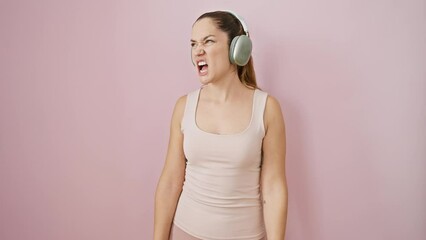 Canvas Print - Furious young woman in sportswear, mad over a rage-aggressive fight, screams out her frustration, blue eyes flashing, headphones discarded. isolated on pink, bristling with frustrated anger.