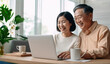 © 18042011 - Smiling Asian Senior couple engaged in happy conversation using laptop for online communication.