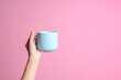 Female hand holding blue cup hot coffee mockup isolated on pink background