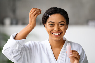 Wall Mural - Beauty Care. Smiling Attractive Black Woman Applying Face Serum With Dropper