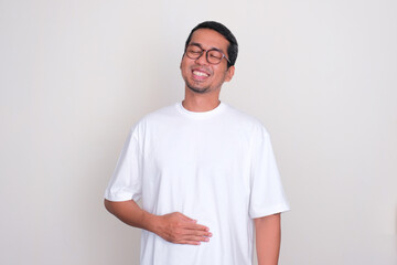 Wall Mural - Adult Asian man smiling happy with one hand touching his stomach