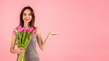 Smiling Woman In A Sparkling Dress Presenting With An Open Hand Gesture While Holding A Bouquet