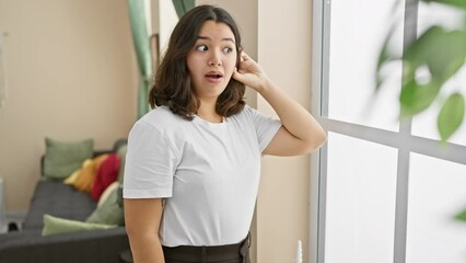 Canvas Print - Gossip time at home, young beautiful hispanic woman, hand over ear, tuning into the rumor mill. standing tall amid whispers, she's all ears, listening keenly despite her deafness.