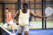 © JackF - Portrait of sporty adult african american man playing padel on indoor court, ready to hit ball. Sport and active lifestyle concept.