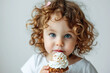 Adorable little girl with curly hair holding a cupcake with whipped cream.