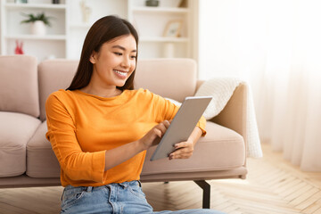 Closeup smiling asian lady holding digital tablet, home interior