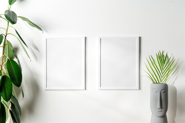 Blank white frames and houseplant against white wall