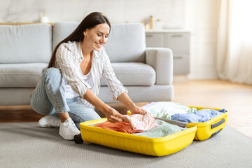 Getting Ready For Travel. Beautiful young woman packing suitcase at home