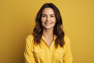 Portrait of happy smiling young woman in yellow shirt, over yellow background