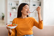 © Prostock-studio - Attractive young asian woman eating vegetable salad at home