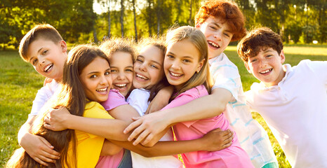 Happy children having fun on summer vacation. Group of best friends playing outdoors together. Several little kids, girls and boys with backlit hair, hugging each other tightly in a green sunny park