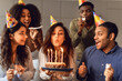 © Prostock-studio - Multiracial friends looking at bday woman blowing out candles indoor