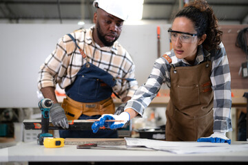 Female Latin carpenter and multiracial colleague working in carpenter's shop repair build wood furniture. Hispanic woman job in woodwork workshop. Diverse ethnic handyman in craft improvement service