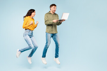 Dynamic couple jumping with joy and a laptop, expressing success