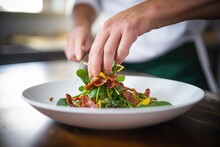 a chefs hand garnishing a finished spinach and bacon salad with herbs