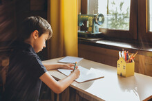 Boy Is Writing A Letter At The Table In His Room In Front Of The Window