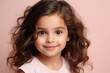 Portrait of a beautiful little girl with long curly hair on a pink background