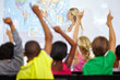 © peopleimages.com - Back of students, teacher and raise hands for questions, education or learning with geography quiz in classroom. Youth, group of kids and school for teaching support, map ideas and answer or test