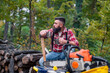 © DusanJelicic - Caucasian man, a lumberjack, takes a moment to rest on a pile of firewood, pouring himself a cup of coffee from a thermos, his tools laid out in front of him.