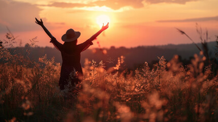 Silhouette photo of one woman standing in outdoor grasses field raising two hands in the air showing freedom relax emotion at twilight time with beautiful sunset.