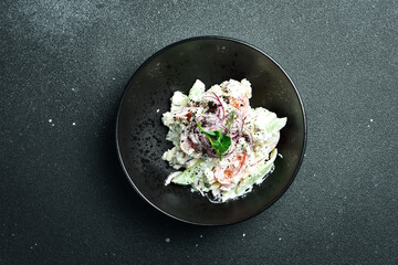 Wall Mural - Salad of cabbage, tomatoes, onions and radish dressed with sour cream. On a plate. Restaurant serving. Close up. On a dark stone background.