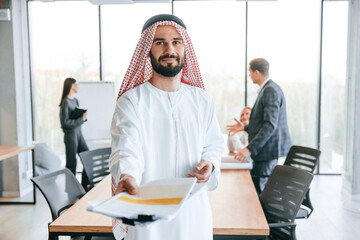 People behind Muslim businessman that is in traditional outfit with colleagues in office