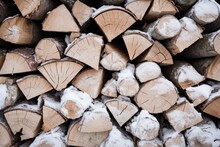 Firewood Stacked In A Snowy Woodpile With Icy Snowflakes.