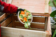 Main d'homme gantée vidant ses épluchures et déchets végétaux dans un composteur neuf en bois vide