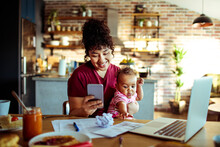 Smiling mother holding baby and using smartphone at home