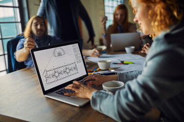 Wall Mural - Focused businesswoman working on laptop with colleagues in background at office