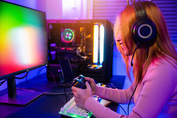 Canvas Print - Gamer using joystick controller for virtual tournament plays online video game with computer neon lights, woman wear gaming headphones playing live stream esports games console at home