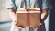 © Viacheslav - Woman's hands holding  present wrapped in craft packing paper with brown ribbon and bow. Stylish gift box a neutral color. Modern minimal present suitable for any occasion. copy space
