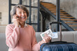 © InsideCreativeHouse - Cheerful old elderly senior happy traveler grandmother woman with airline train tickets calling taxi to airport train station, moving abroad to a new place country for holidays