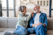 Cheerful caucasian senior old elderly couple spouses grandparents hugging embracing cuddling, spending time together while relaxing resting on the sofa couch