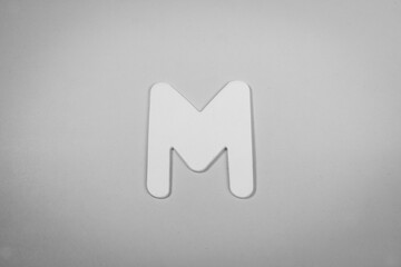 Letter M in wood on a pink background (black and white)