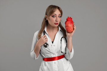 Poster - Woman in scary nurse costume with heart model on light grey background. Halloween celebration