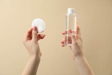 Wall Mural - Woman holding makeup remover and cotton pad on beige background, closeup